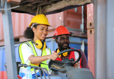 Two workers, a man and a woman, operating a forklift together in a warehouse